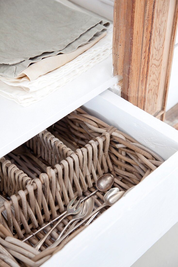 Open drawer with wicker cutlery tray and small stack of linen cloths