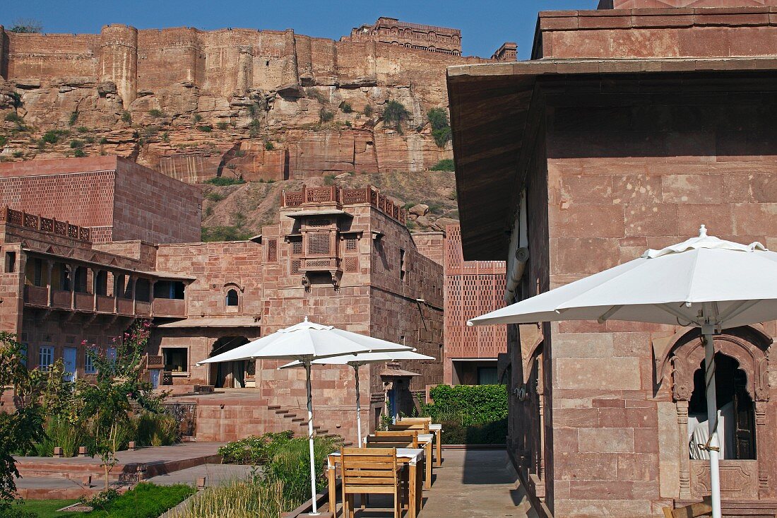 Outside view of Raas Haveli Hotel, Jodhpur, India with parasols, restaurant tables, gardens and view of mountain fortress