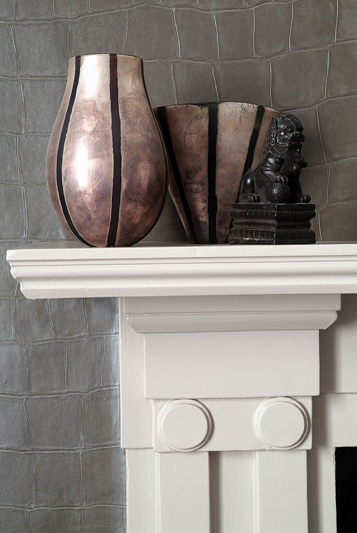 Different vases on mantelpiece against leather-covered wall