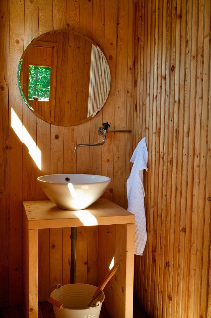 Holzverkleidetes Bad mit schlichtem Waschtisch und rundem Spiegel an Wand