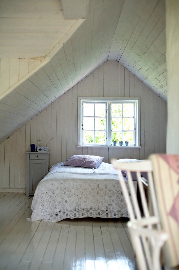Weisses holzverkleidetes Schlafzimmer im Dachgeschoss eines schlichten Holzhauses