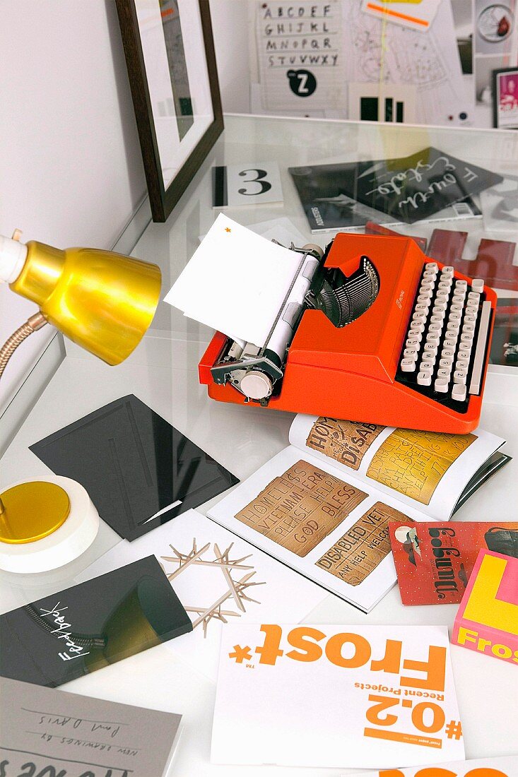 Orangefarbene Schreibmaschine und goldene Tischlampe auf Schreibtisch