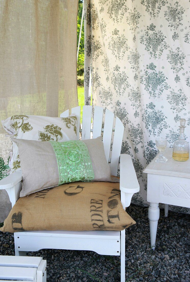 Various cushions on white-painted garden chair against floral interior wall of tent