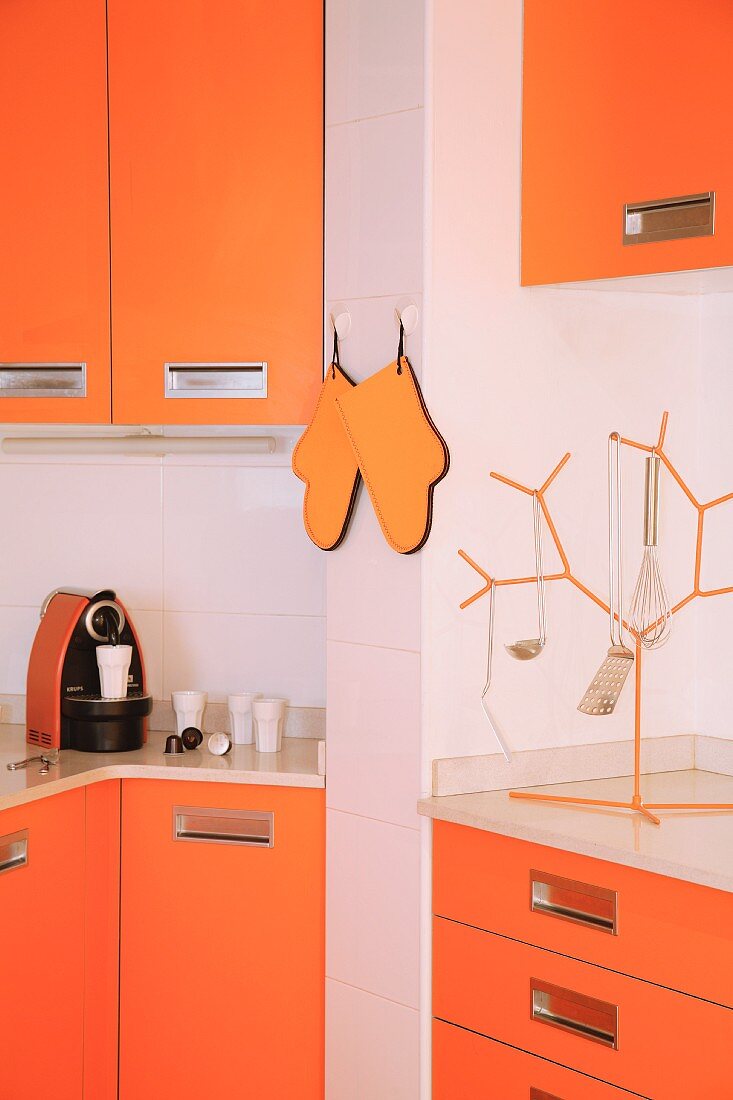 Fitted kitchen with orange fronts, orange oven gloves and matching tree-shaped rack for hanging utensils
