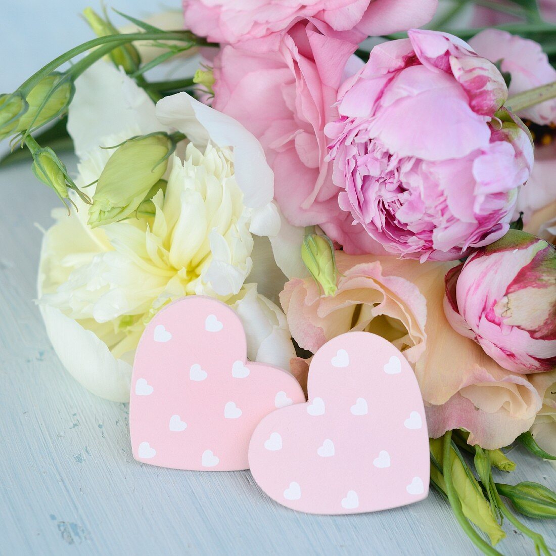 Two pink decorative hearts in front of bouquet (peonies)