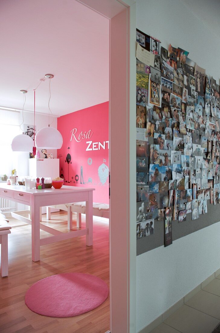 Blick vom Flur mit grosser Fotosammlung an der Wand in pinkfarbenen Essraum mit weisser Esstafel und rosafarbener Fussmatte