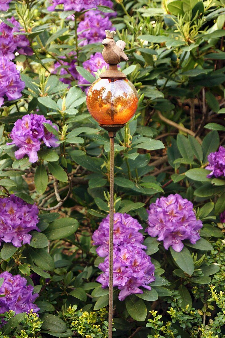 Ball stake with bird figure in front of purple-flowering rhododendron