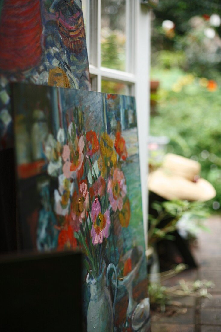 Ölbilder mit Blumenmotiv gestapelt vor offener Terrassentür und Blick in Garten