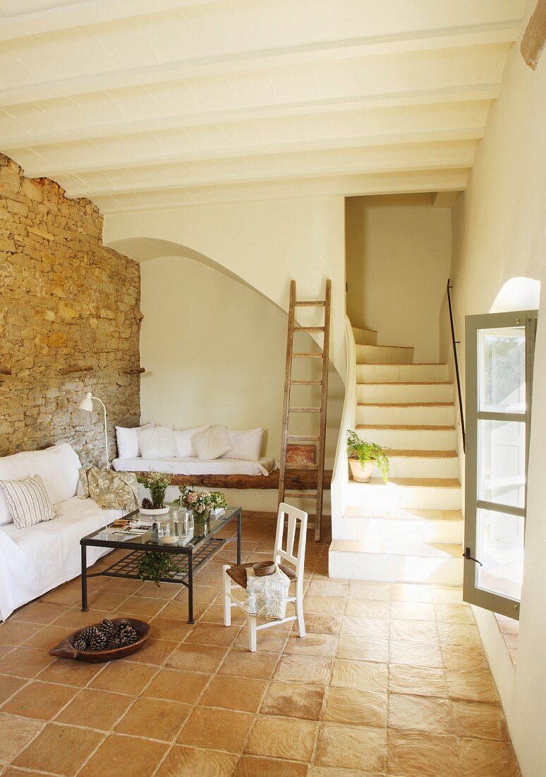 Einfacher, mediterraner Wohnraum mit Terracottafliesen und gemauertem Treppenaufgang