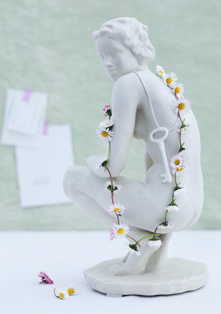 weiße Keramikfigur mit umgehängtem Schlüssel und Kette aus Gänseblümchen