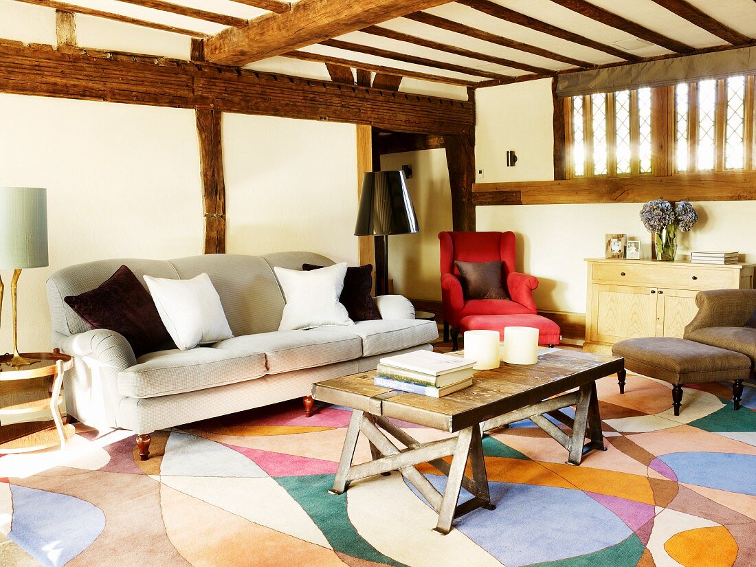 Rustic coffee table and antique sofa on patterned carpet in house with wooden half-timbered structure