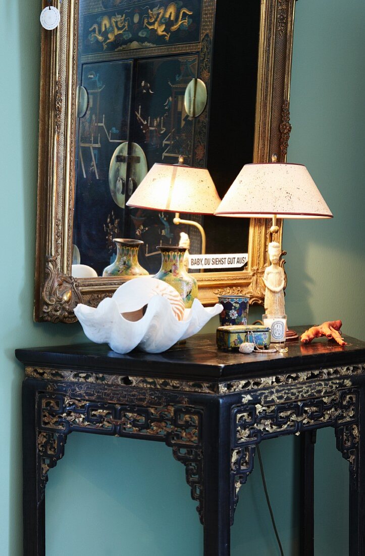 Gilt-framed mirror on wall and collectors' items on ornate, lacquered table