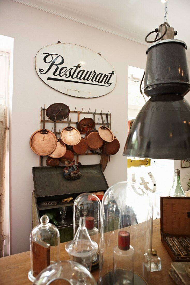 Altes Restaurant-Schild mit einer darunterhängenden Sammlung glänzender Kupferpfannen; im Vordergrund mehrere Glasglocken