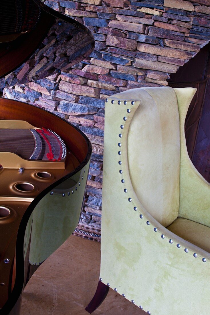 Stone wall behind open grand piano lid and elegant leather armchair