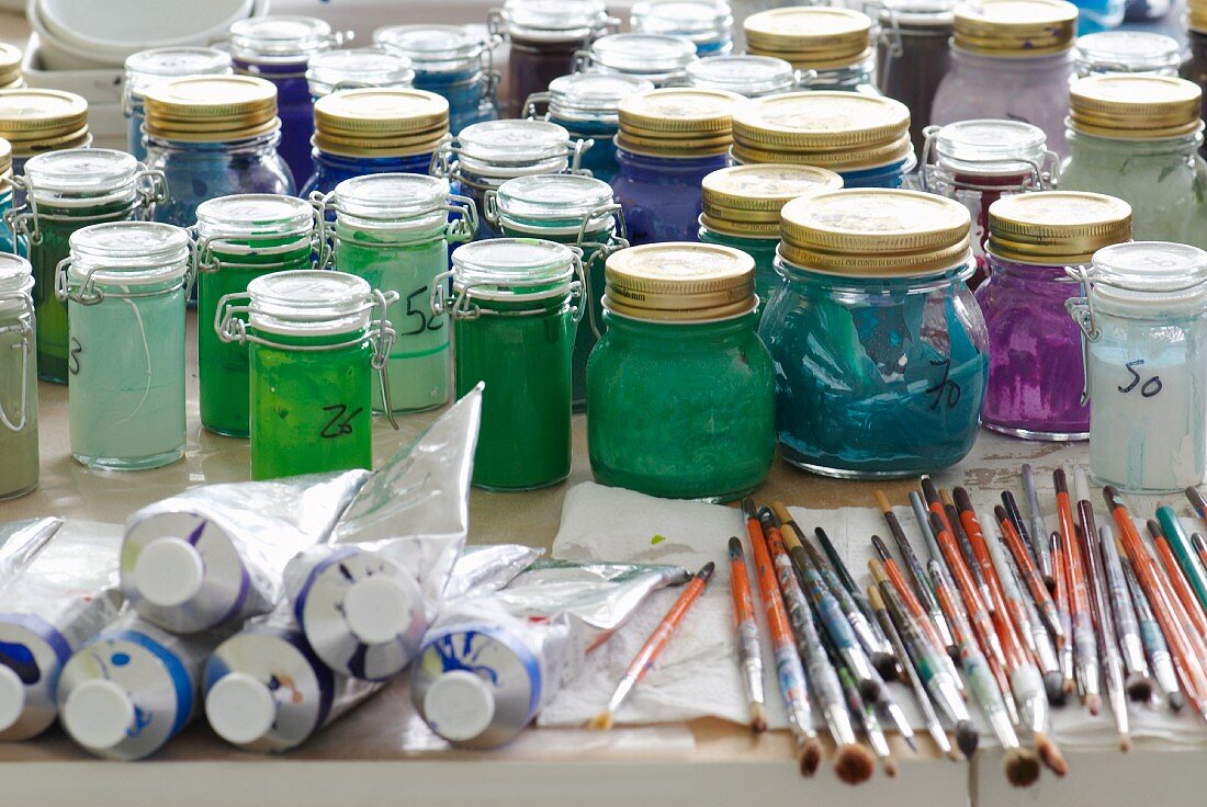 Arbeitstisch eines Künstlers: Farbtuben, Pinsel und Glastöpfe mit zahlreichen Farben