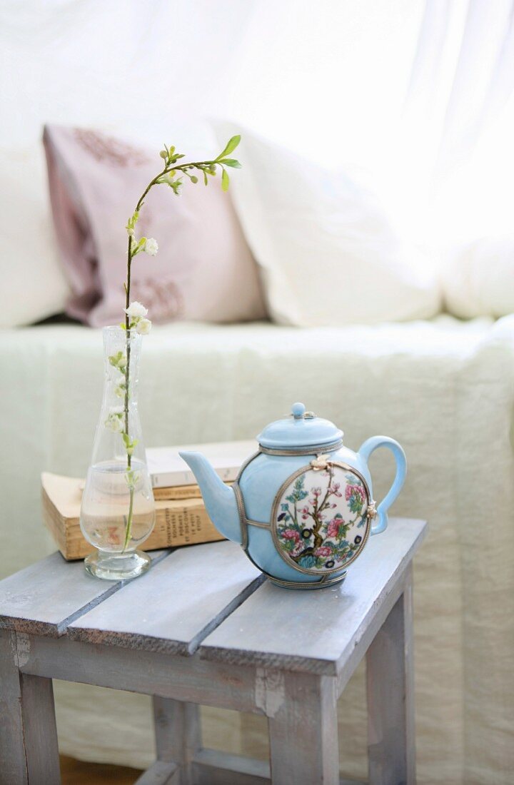 Asiatische Teekanne, blühender Zweig und Bücher auf einem Hocker neben dem Bett