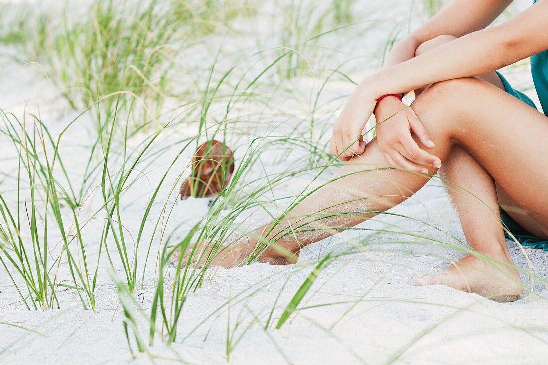 Weiblicher Teenager sitzt am Sandstrand zwischen Gräsern