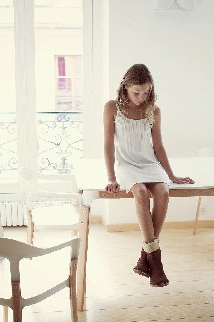 Girl wearing dress and boots sitting on table in room