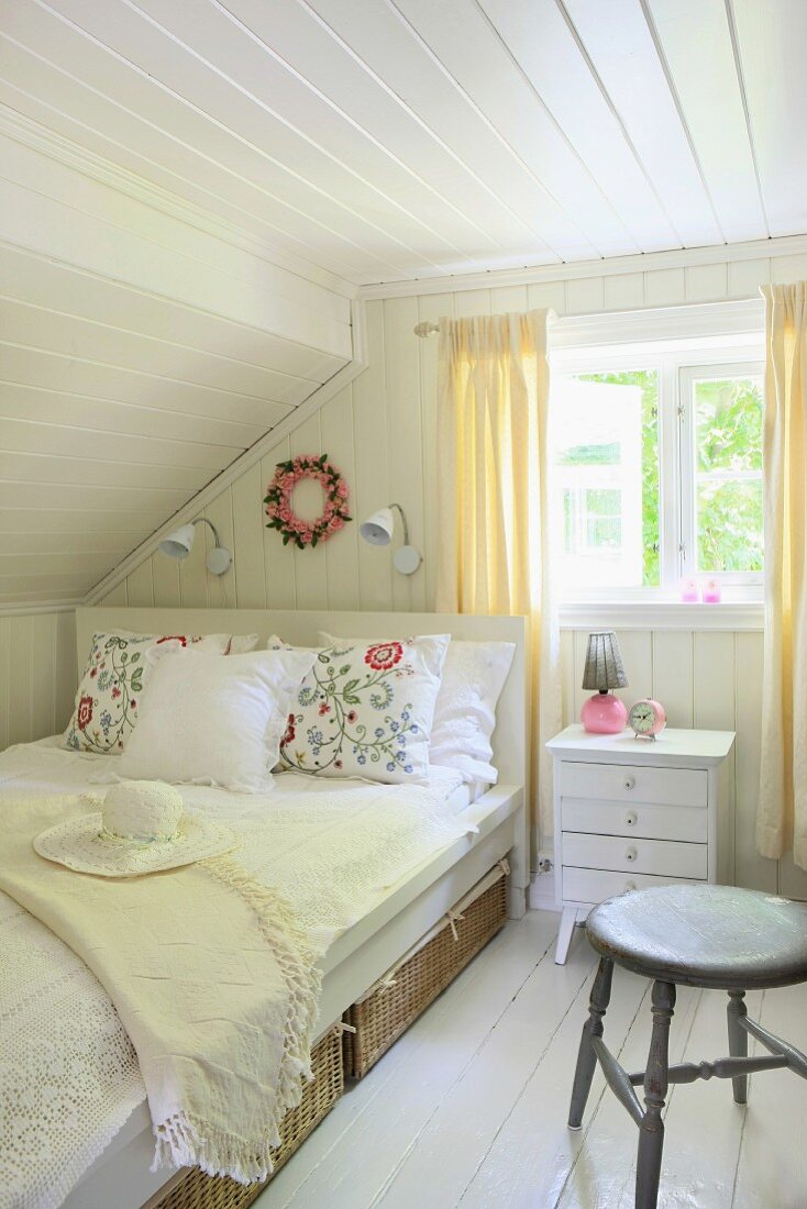 Luftiges Schlafzimmer mit Körben als Unterbettkommoden und fröhlich bestickten Kissen
