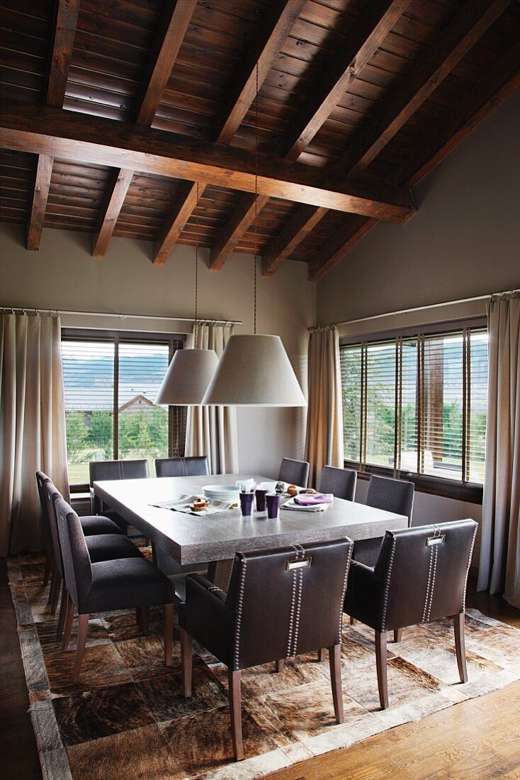 Spacious dining area with patchwork, animal skin rug and comfy, upholstered chairs under a dark wood beam ceiling