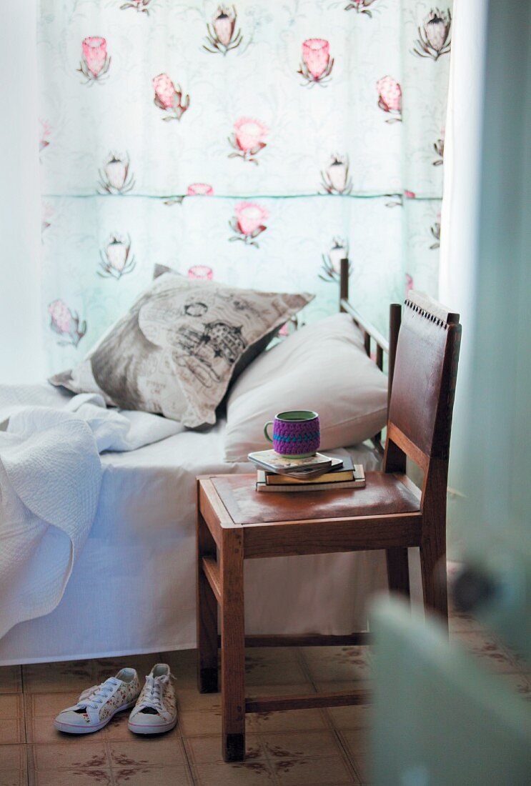 Schlafzimmer mit Einzelbett, geblümten Vorhängen, Dekokissen und Lederstuhl als Nachtkästchen