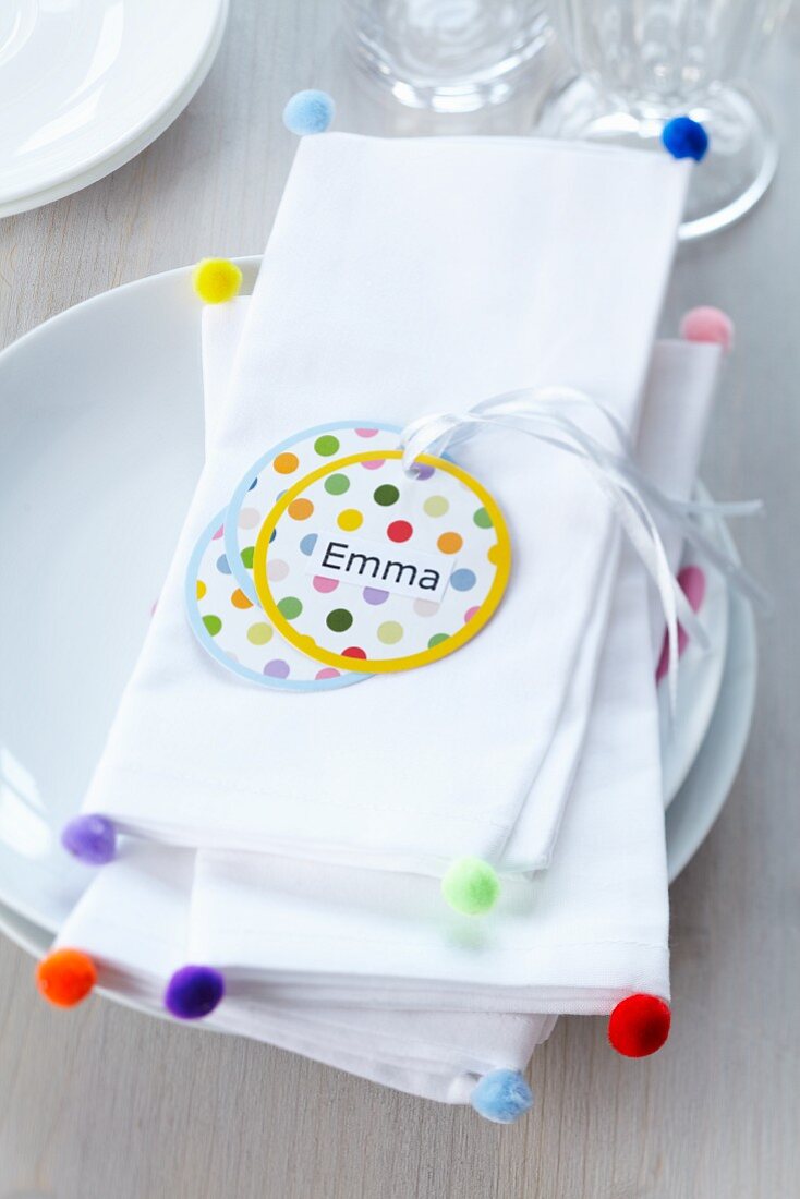 White linen napkins decorated with colourful miniature pompoms & name tags