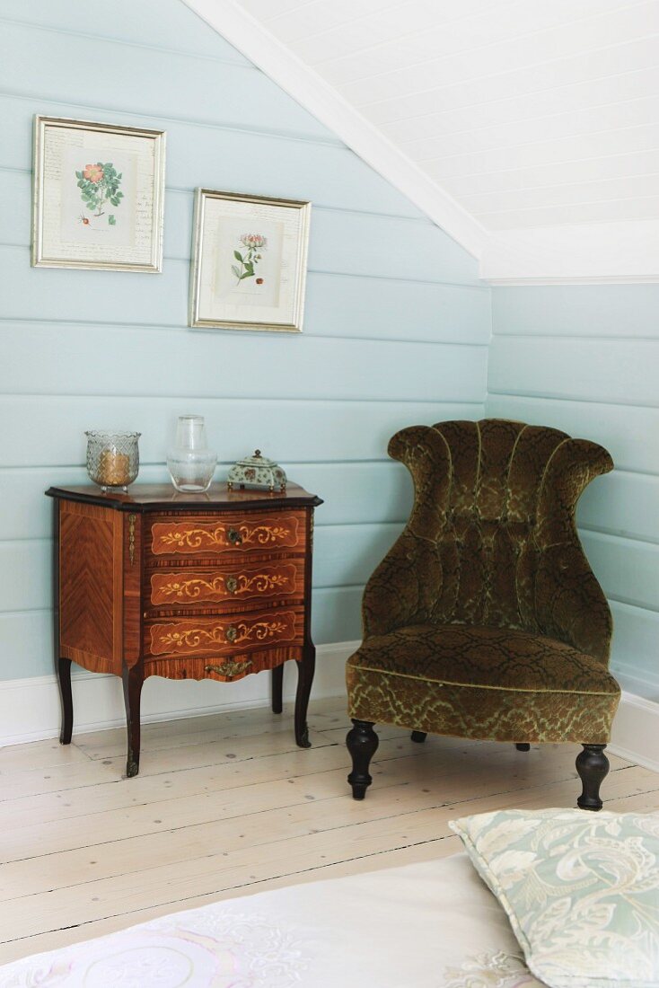 Pale blue wall panelling, antique chest of drawers and upholstered armchair in attic bedroom