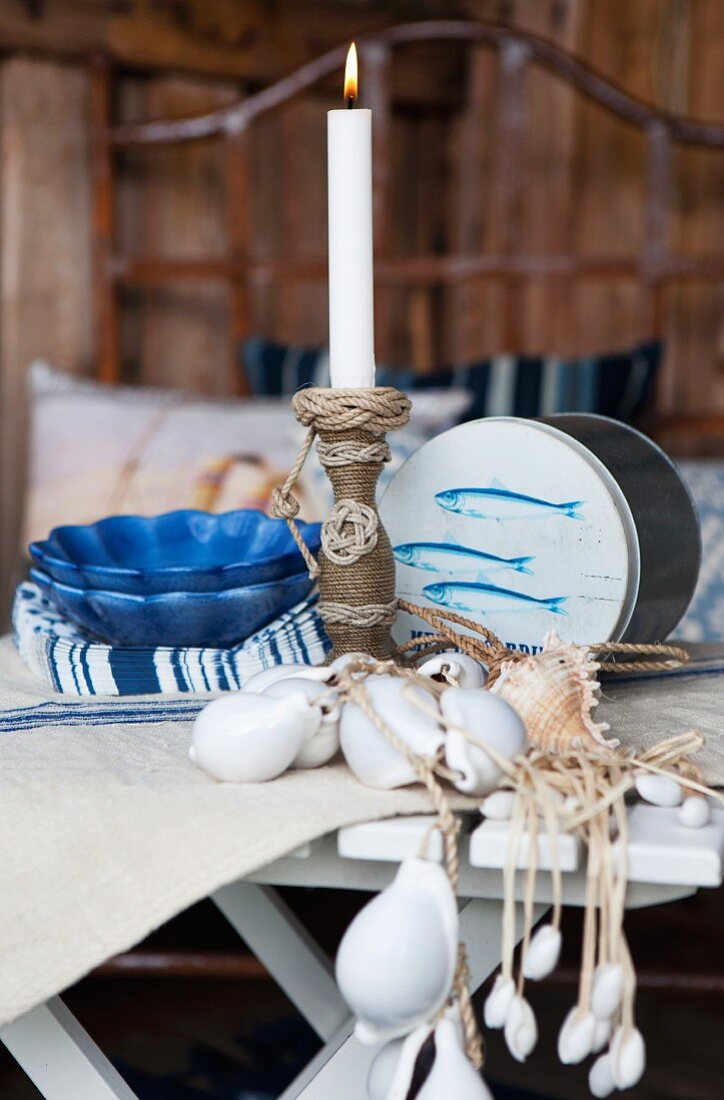 Handgearbeiteter Kerzenständer aus gewickeltem Seil, blaue Schalen und Muschelketten auf Gartentisch