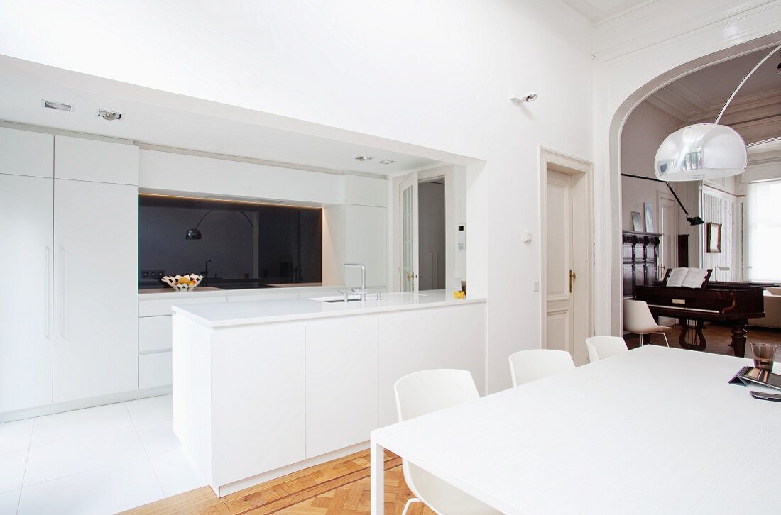 Einbauküche und Esstisch mit Designerstühlen im puristisch weiss gestalteten, offenen Wohn/Essraum einer schicken Altbauwohnung