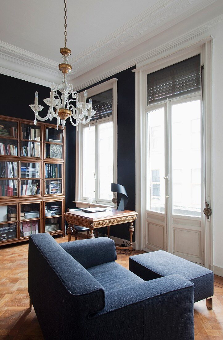 Study in stylish period apartment with antique desk, bookcase and modern, angular two-seater sofa