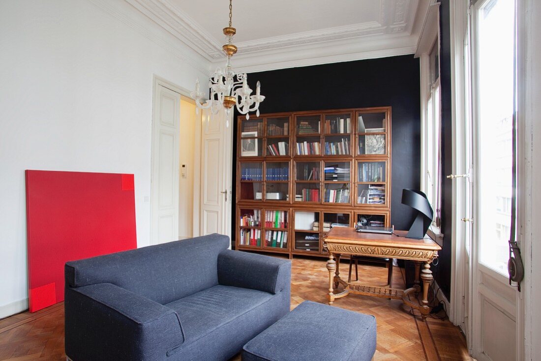 Blue two-seater sofa in front of bright red painting and bookcase in study of grand period apartment