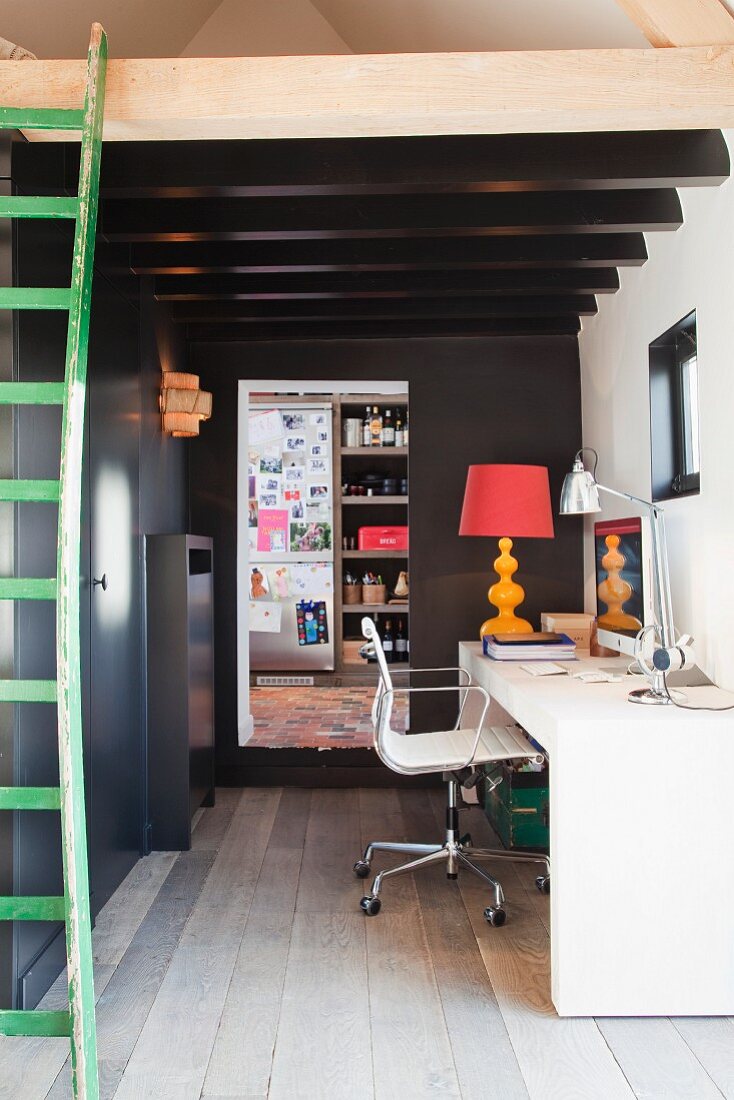 White desk and white Eames swivel chair below dark, wood-beamed ceiling; green vintage ladder in foreground