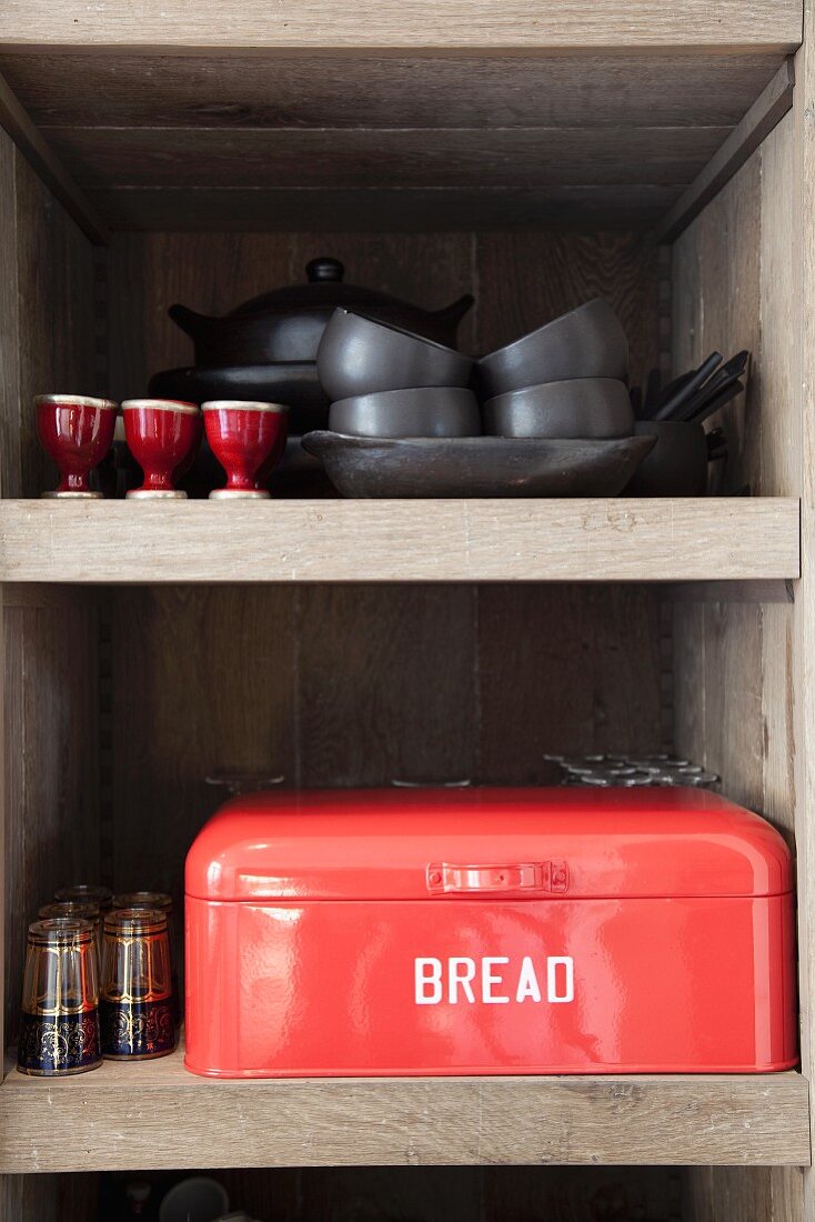 Pans, crockery and red bread bin with lettering on kitchen shelves