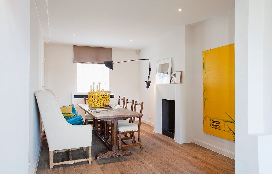 Contemporary dining room with antique, reupholstered armchair, long dining table and monochrome yellow artwork on white wall