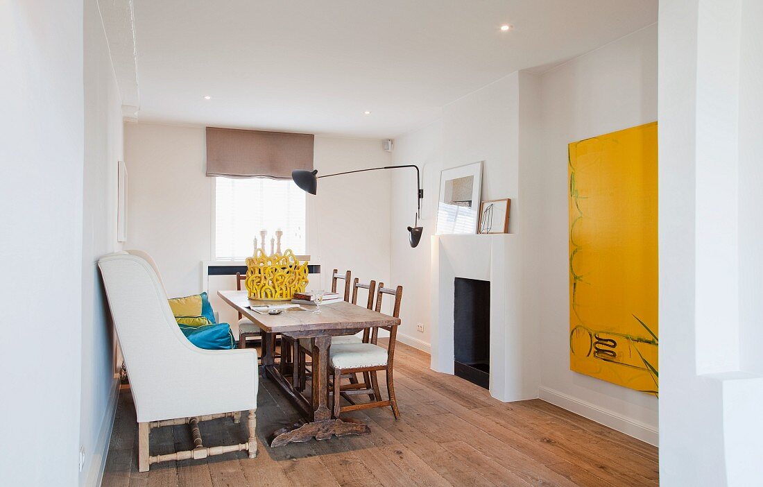 Zeitgenössisches Esszimmer mit antikem, neu bezogenen Sessel, langer Esstafel und einem monochromen Gemälde in Gelb an der weissen Wand