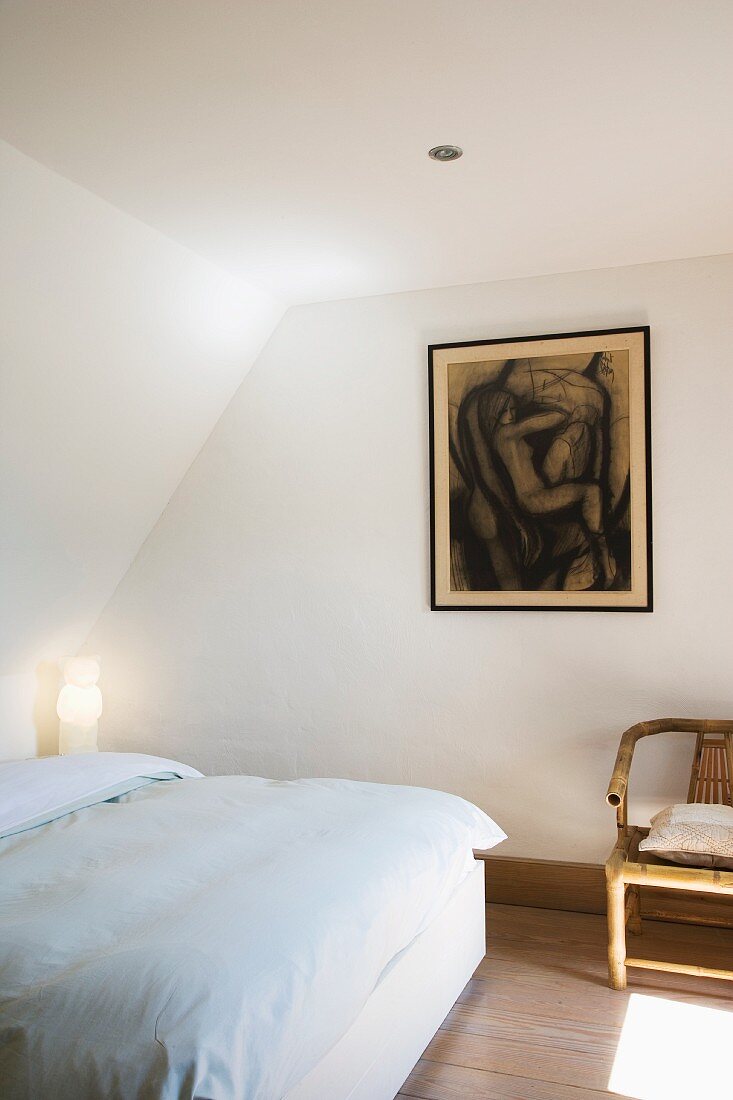 Double bed with white bed line and framed drawing on wall in simple attic room