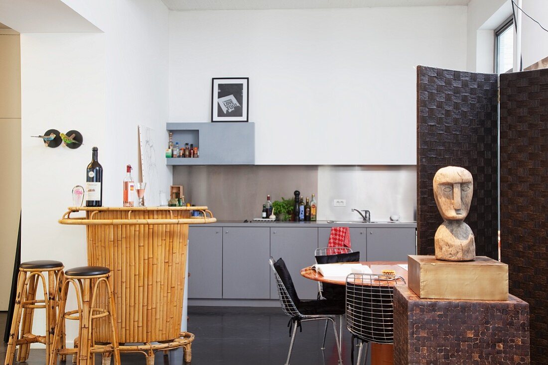 Bamboo bar, dining table, designer chairs and ethnic figurine in front of simple modern kitchen counter in vintage loft