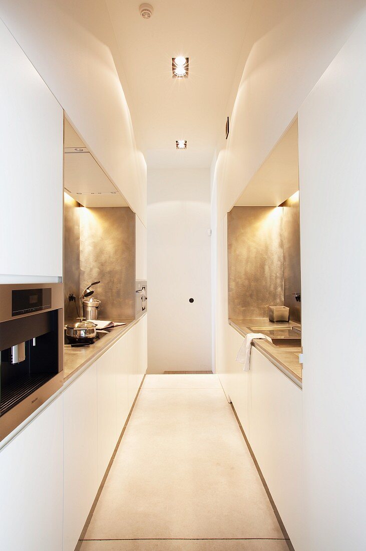 Futuristic designer kitchen - narrow room with white and pale grey installations on both sides and suspended ceiling with recessed spotlights