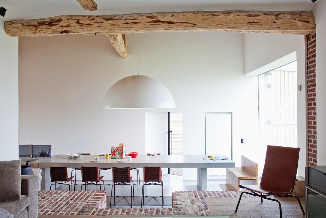 Blick durch breiten Durchgang auf Esstisch mit Stühlen in minimalistischem Wohnzimmer und Boden teilweise aus Ziegelsteinen