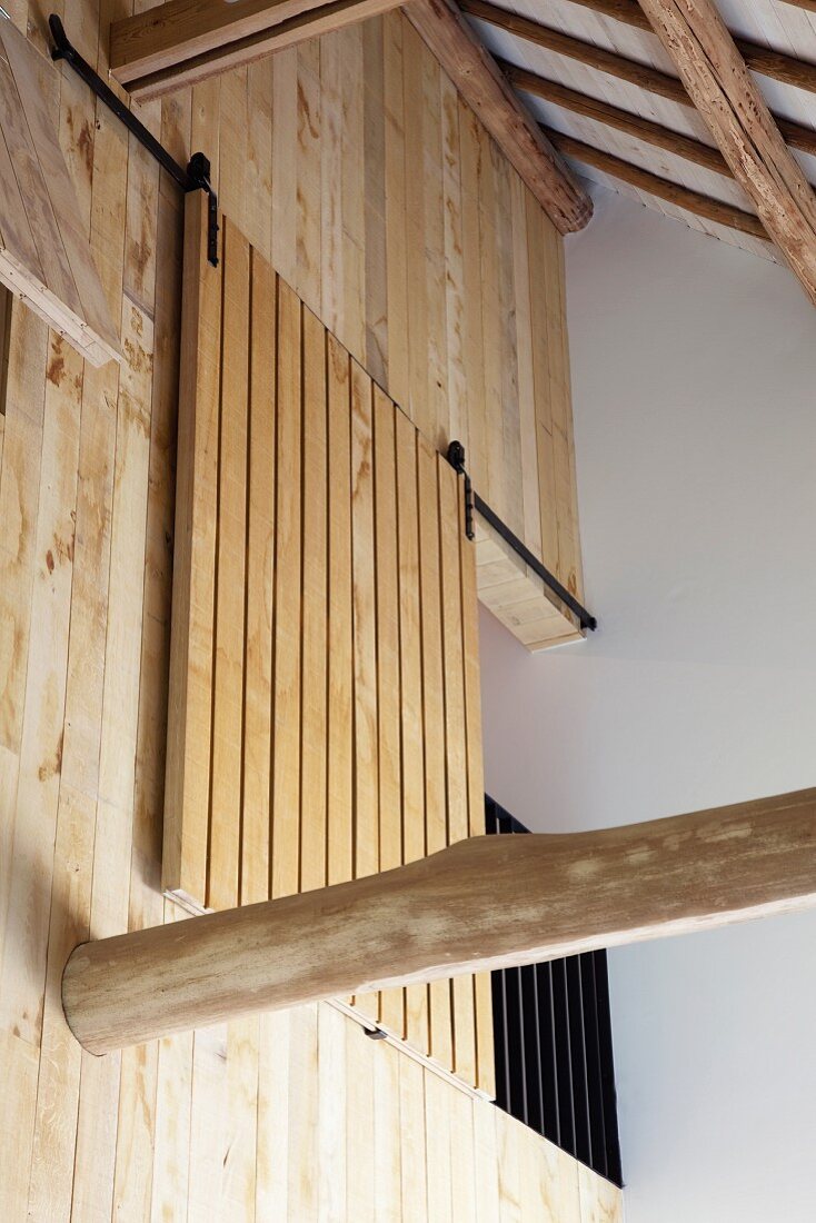 View up to wooden wall with sliding wooden element on gallery with balustrade in roof space