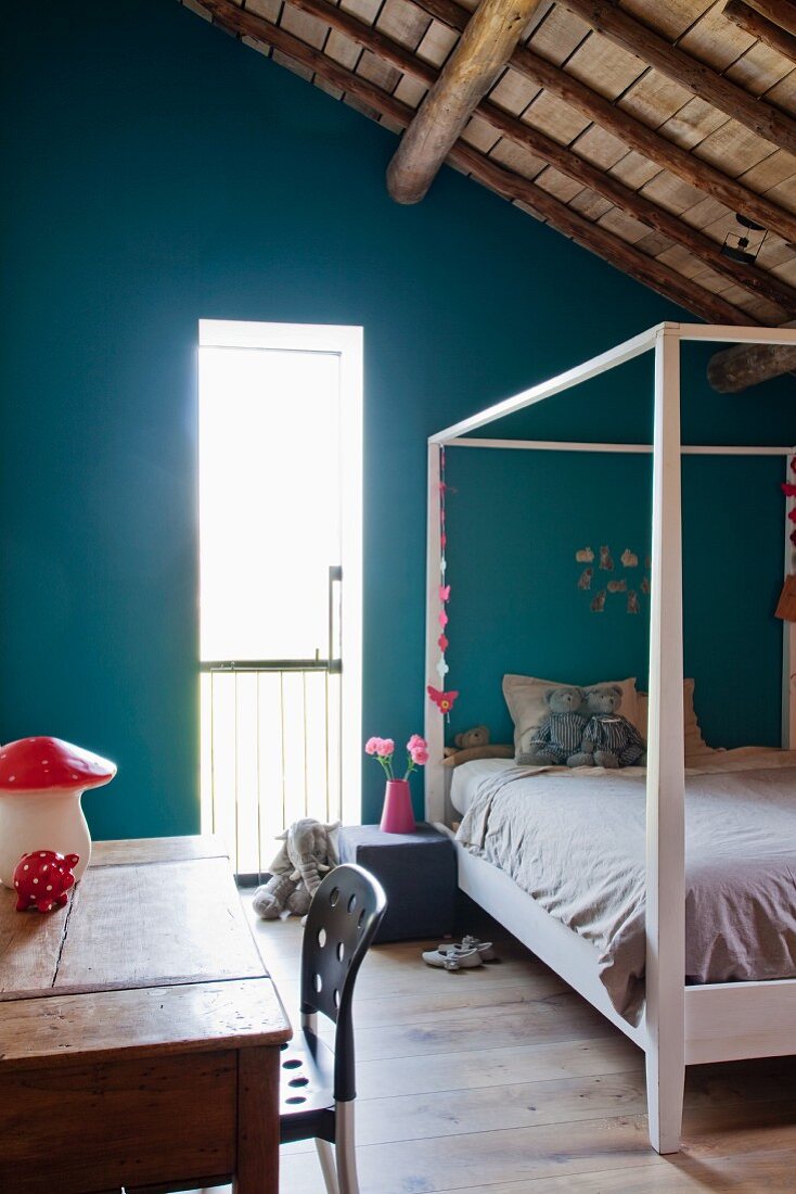 Rustic child's bed with four-poster frame, turquoise wall, table and chair in attic room