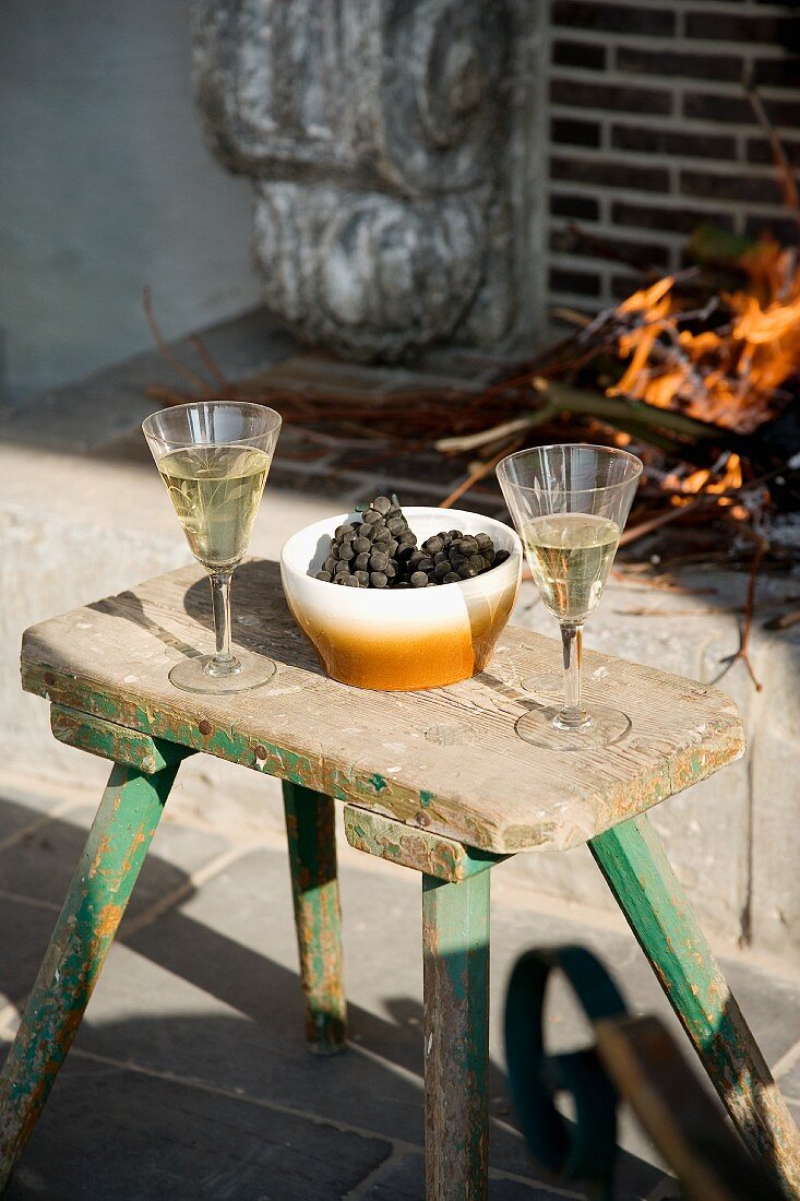 Glasses of white wine and grapes on vintage stool used as side table in front of open fire