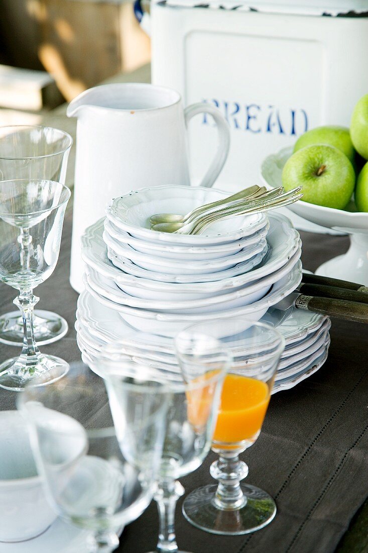 Stack of white crockery, glasses and fruit bowl on brown linen tablecloth