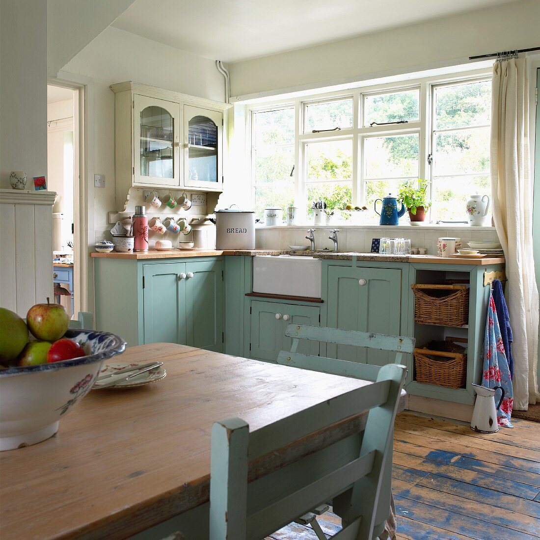 Pastellblaue alte Wohnküche im englischen Landhausstil; Schale mit Äpfeln auf Esstisch im Vordergrund