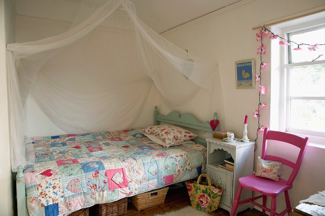 Romantisches Landhausbett mit Patchworkdecke und drapiertem Moskitonetz in Kinderzimmer