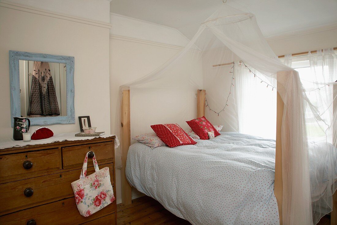 Schlafzimmer im Landhausstil mit altem Schubladenschrank und drapiertem Moskitonetz über dem Doppelbett