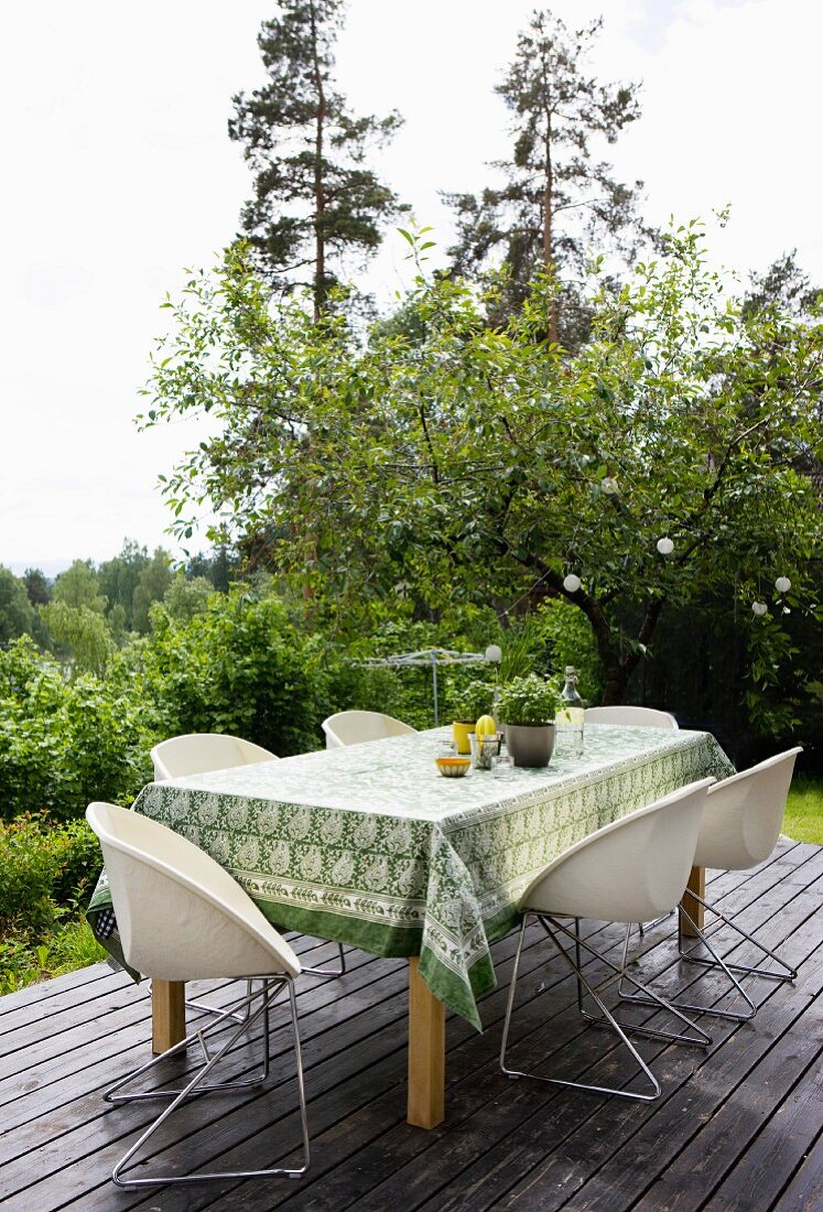 Schalenstühle mit Metallgestell um Tisch mit Tischdecke auf Holzterrasse vor Waldlandschaft