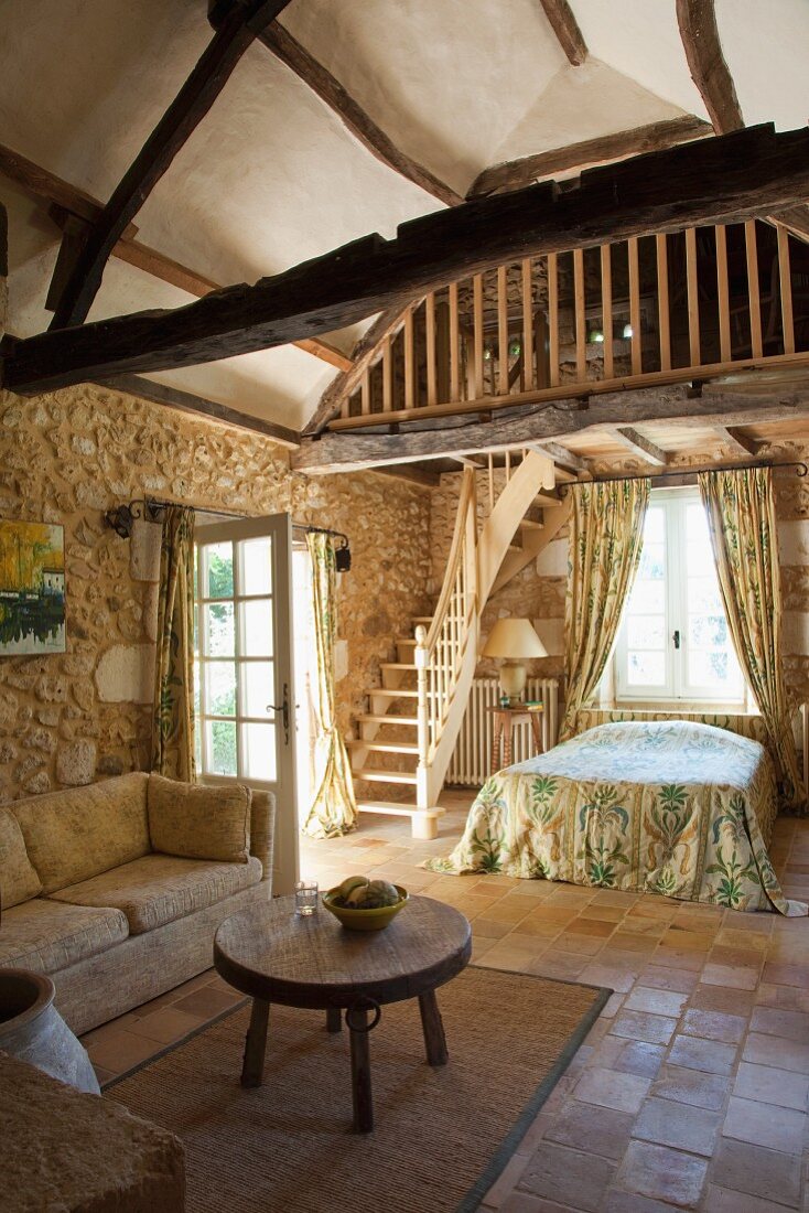 Rustic interior with sofa and side table in front of sleeping area and stairs leading to gallery
