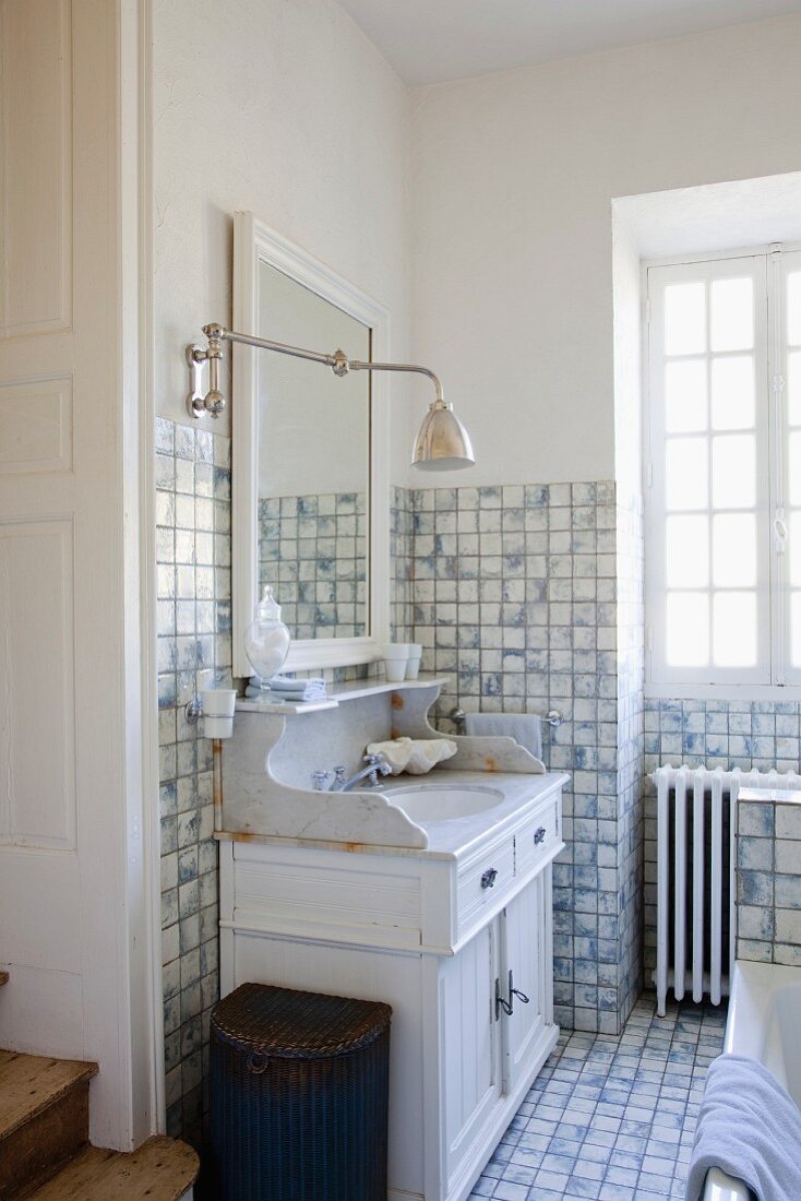 Vintage washstand with marble top below retro sconce lamp in rustic tiled bathroom