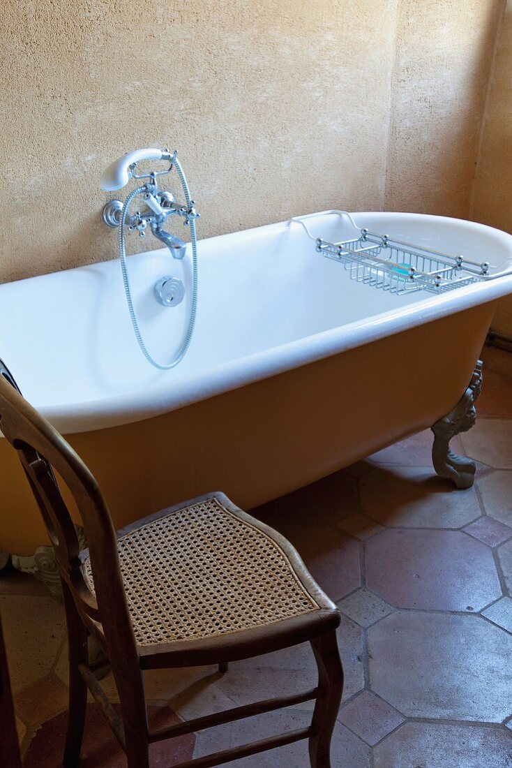 Chair with cane seat next to vintage bathtub in rustic bathroom